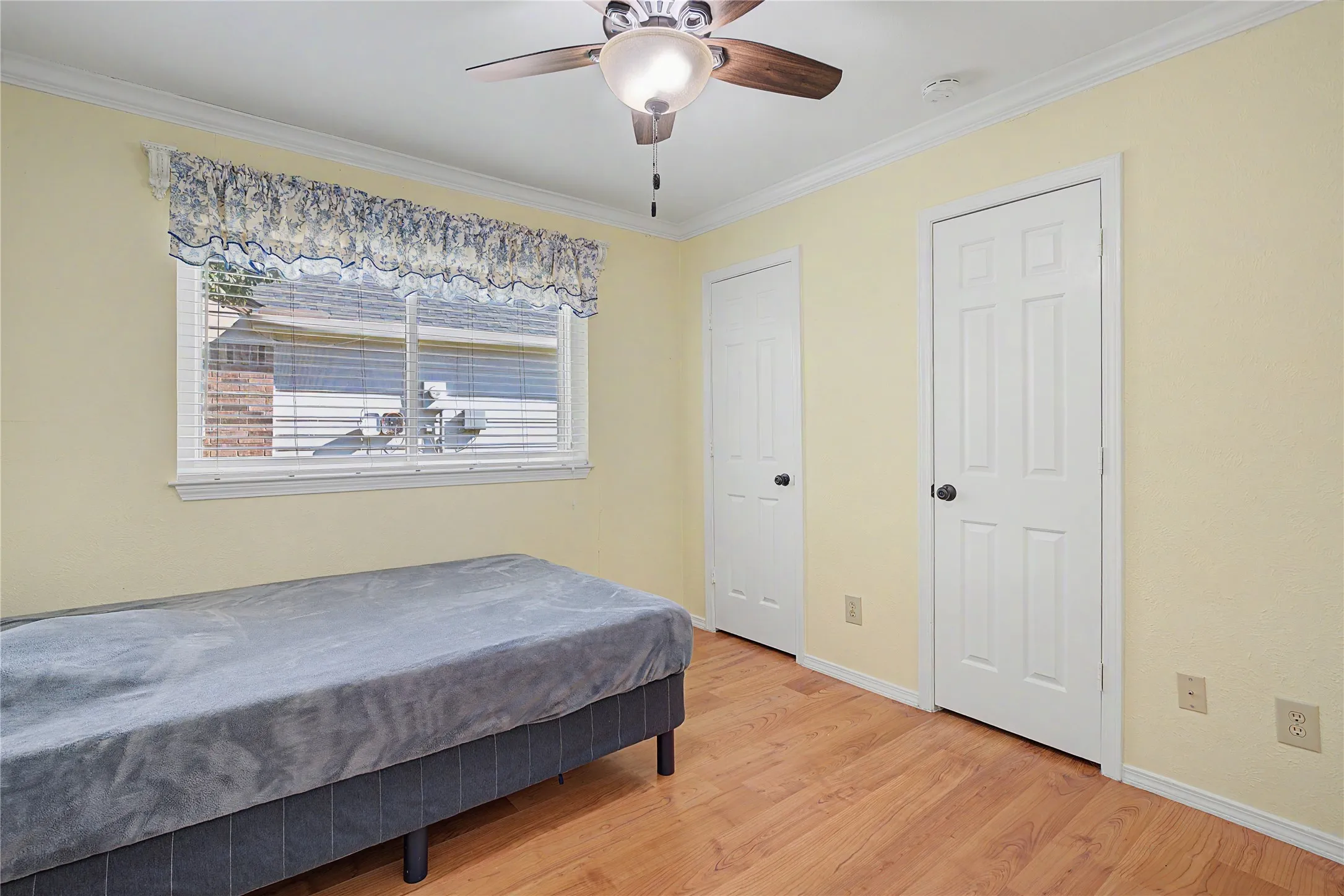 Wood-finish flooring, ceiling fan with integrated lighting, window with blinds, and white paneled doors