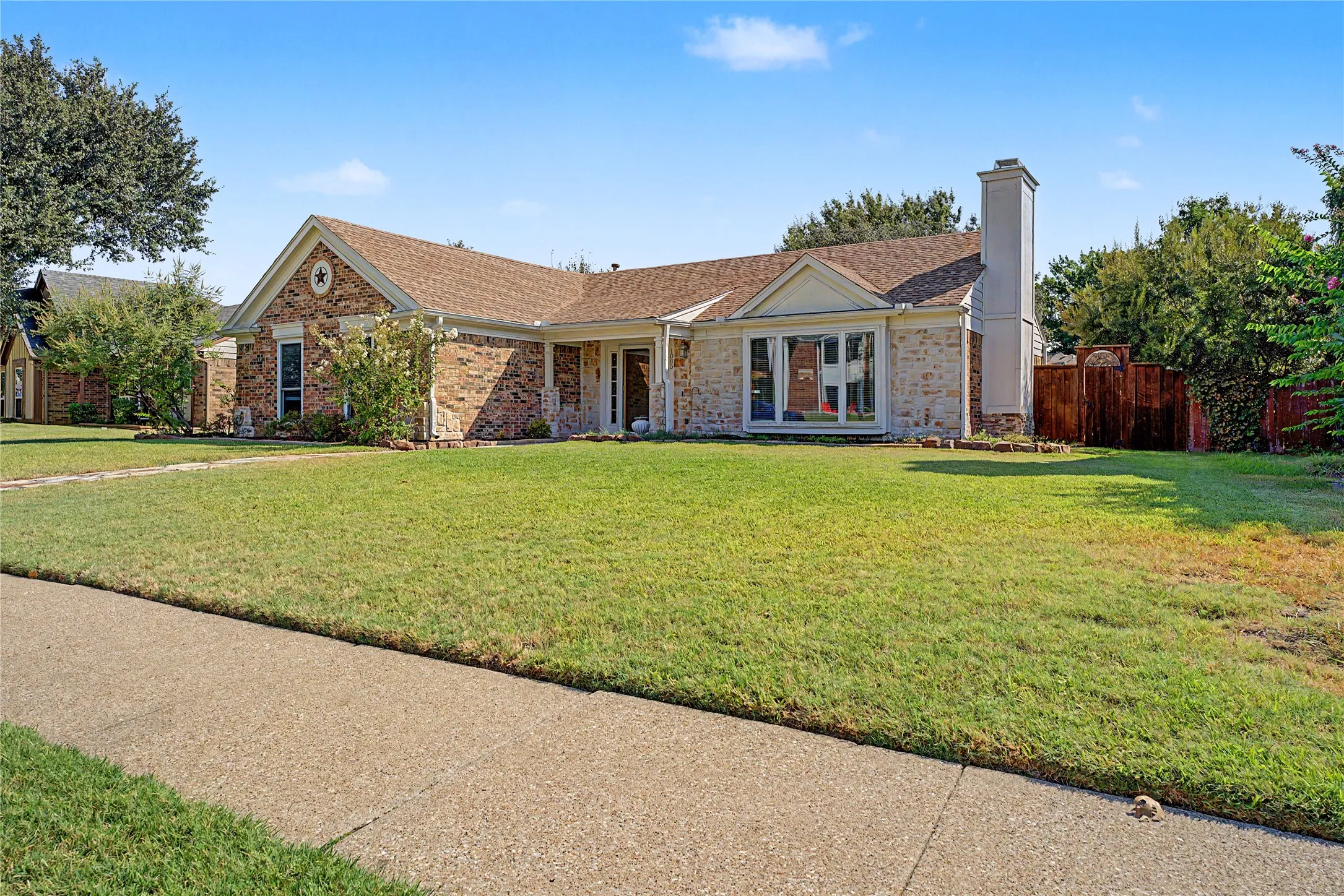 Brick and stone veneer exterior with a prominent chimney, front-facing gable, and a fenced side yard
