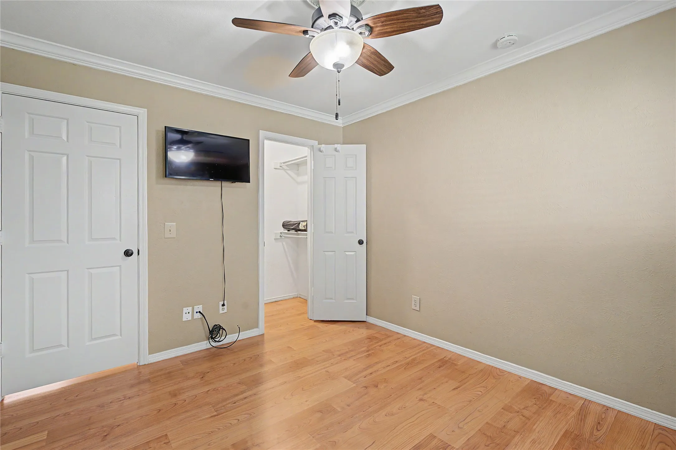 Wood-finish flooring, ceiling fan, crown molding, and white paneled doors