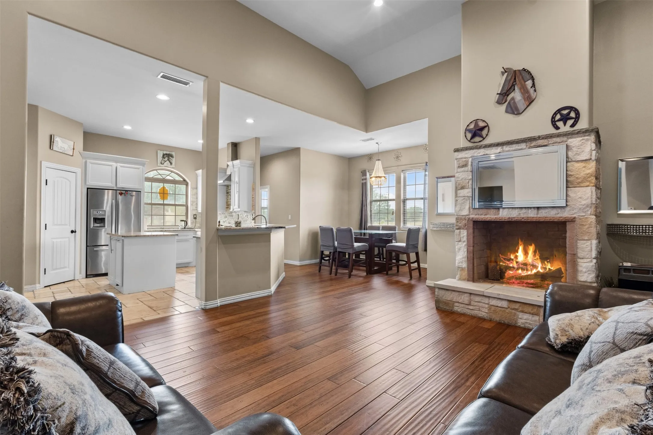 Vaulted ceilings with recessed lighting, wood-finish flooring, a stone-clad fireplace, and a kitchen with white cabinetry and stainless steel appliances