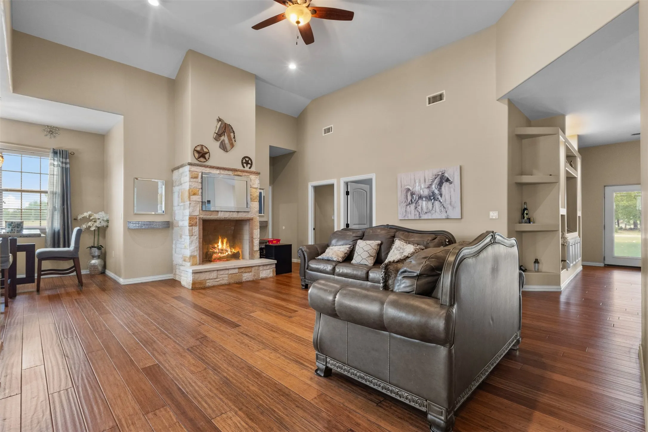 Vaulted ceilings, a stone-clad fireplace, wood-finish flooring, recessed lighting, and built-in shelving