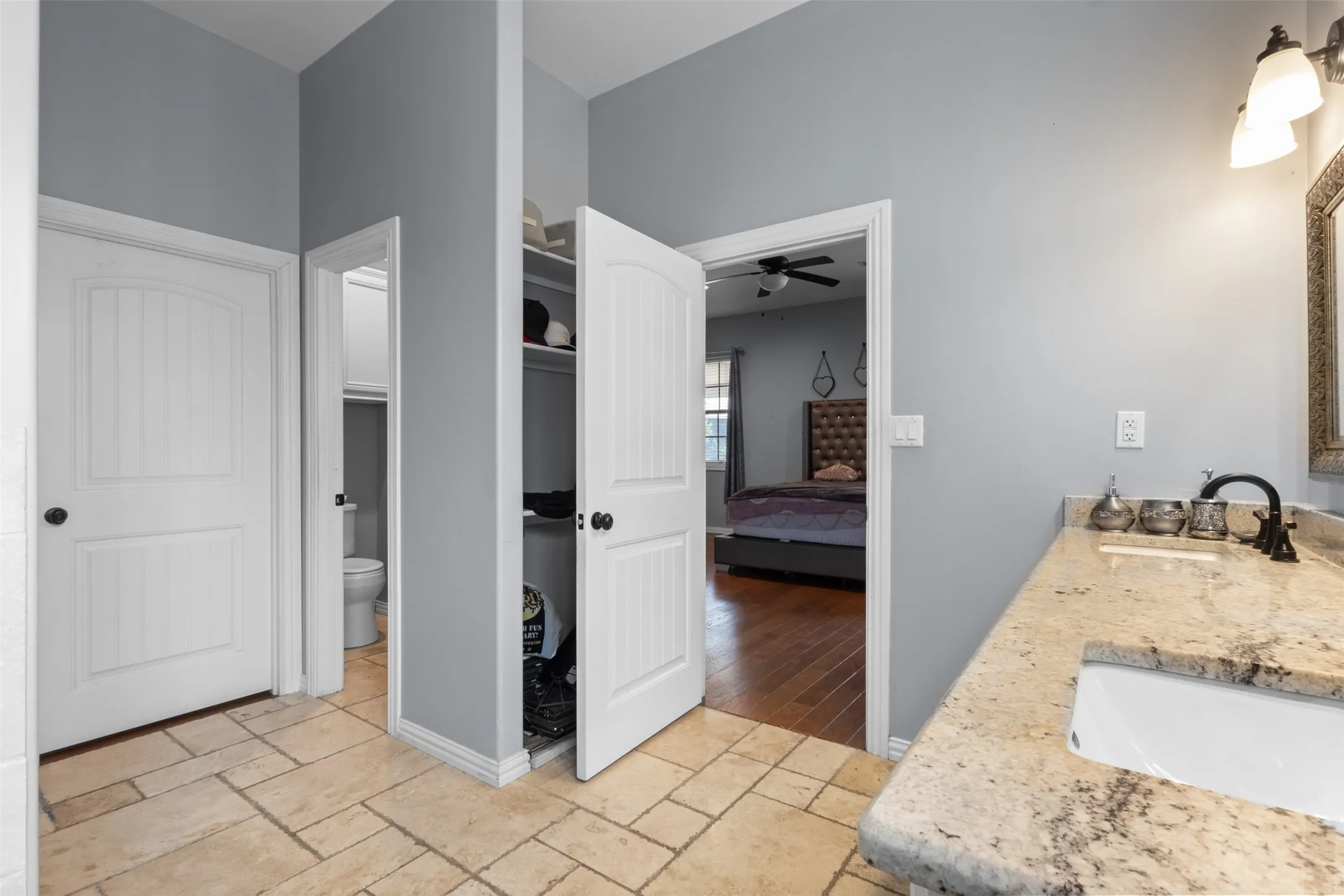 Stone-look tile flooring, light gray wall finishes, recessed shelving, and a vanity with a polished countertop and integrated sink