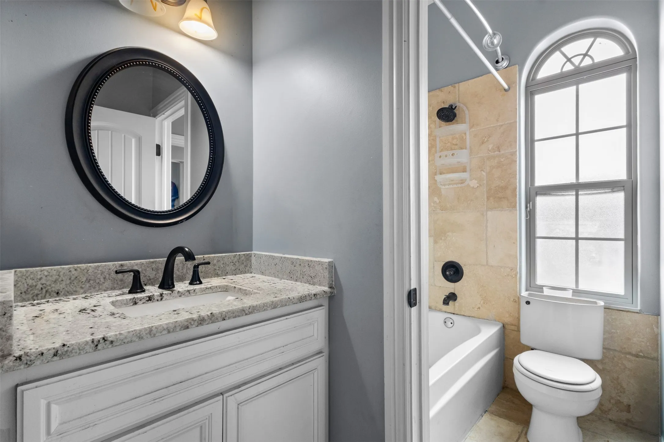 White vanity with stone-finish countertop, black-finish faucet, and a circular framed mirror