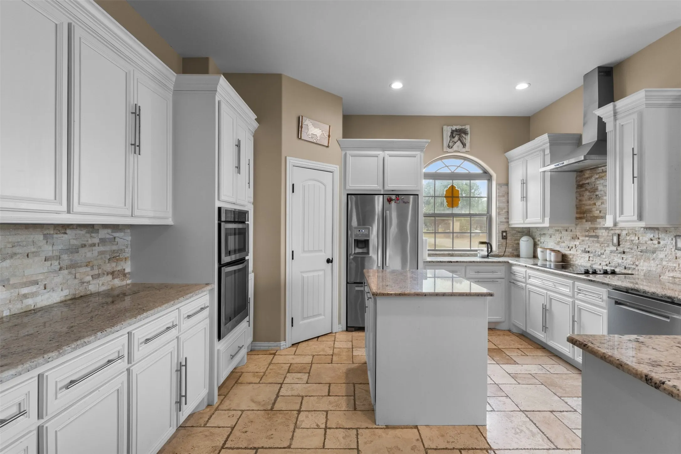 Kitchen featuring white cabinetry, stone countertops, a central island, stainless steel appliances, and tile flooring