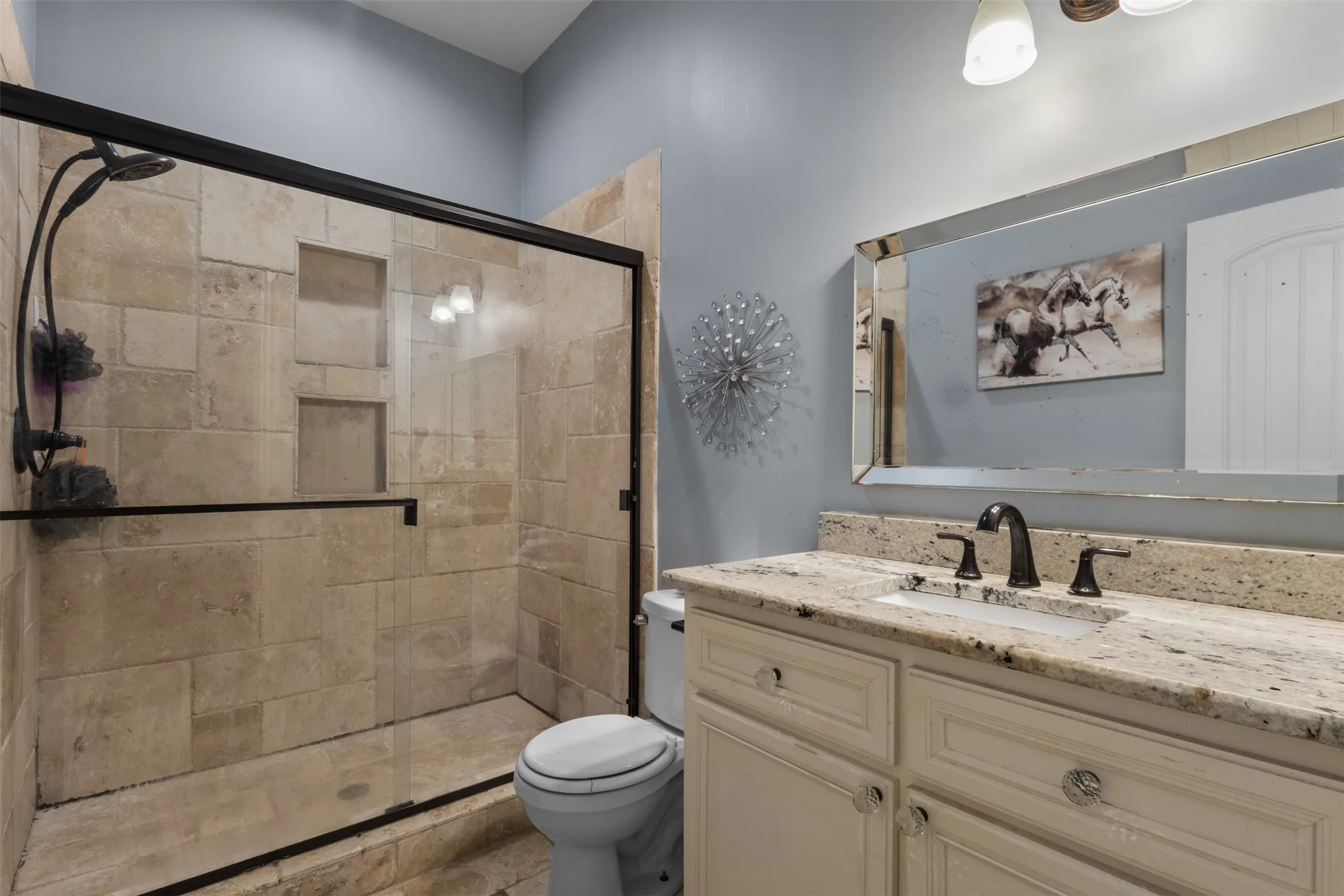 Walk-in shower with tiled walls and glass enclosure, vanity with stone countertop, integrated sink, and an expansive mirror