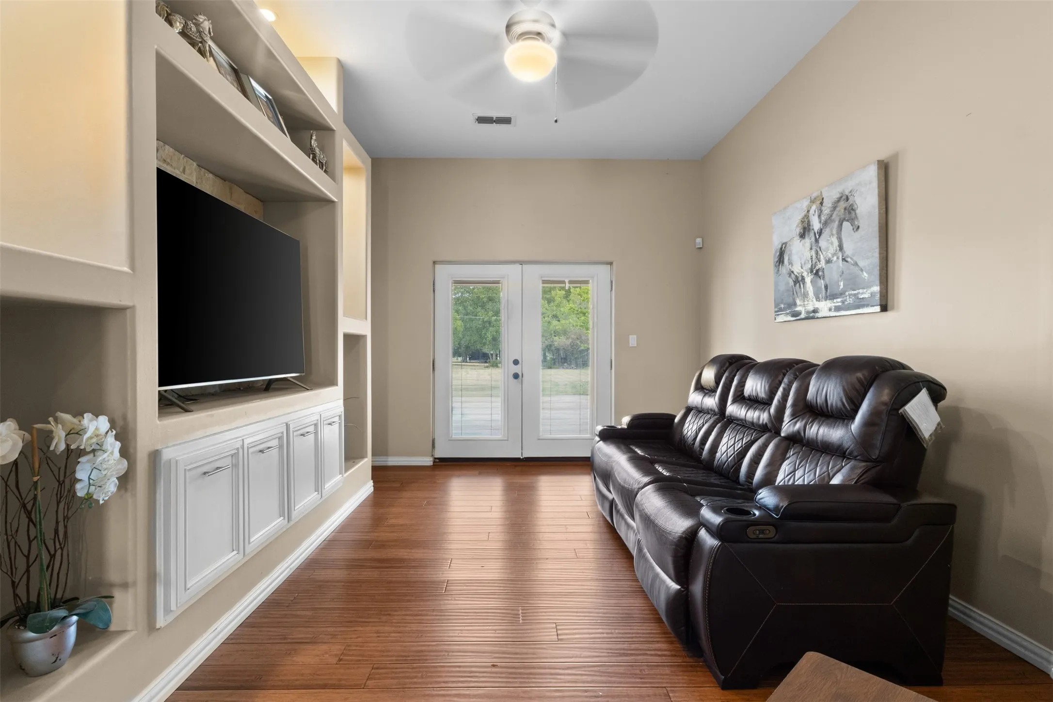 Wood-finish flooring, built-in shelving, integrated cabinetry, vaulted ceiling, and glass-paneled double doors