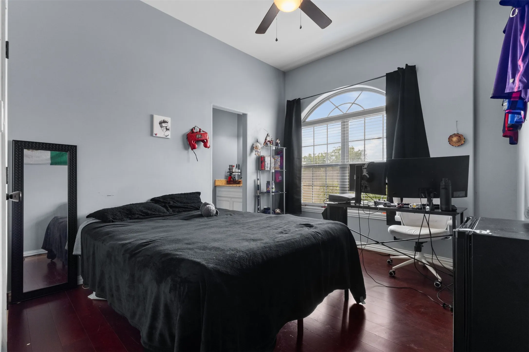 Vaulted ceiling with a ceiling fan, arched window with blinds, wood-finish flooring, and a recessed alcove