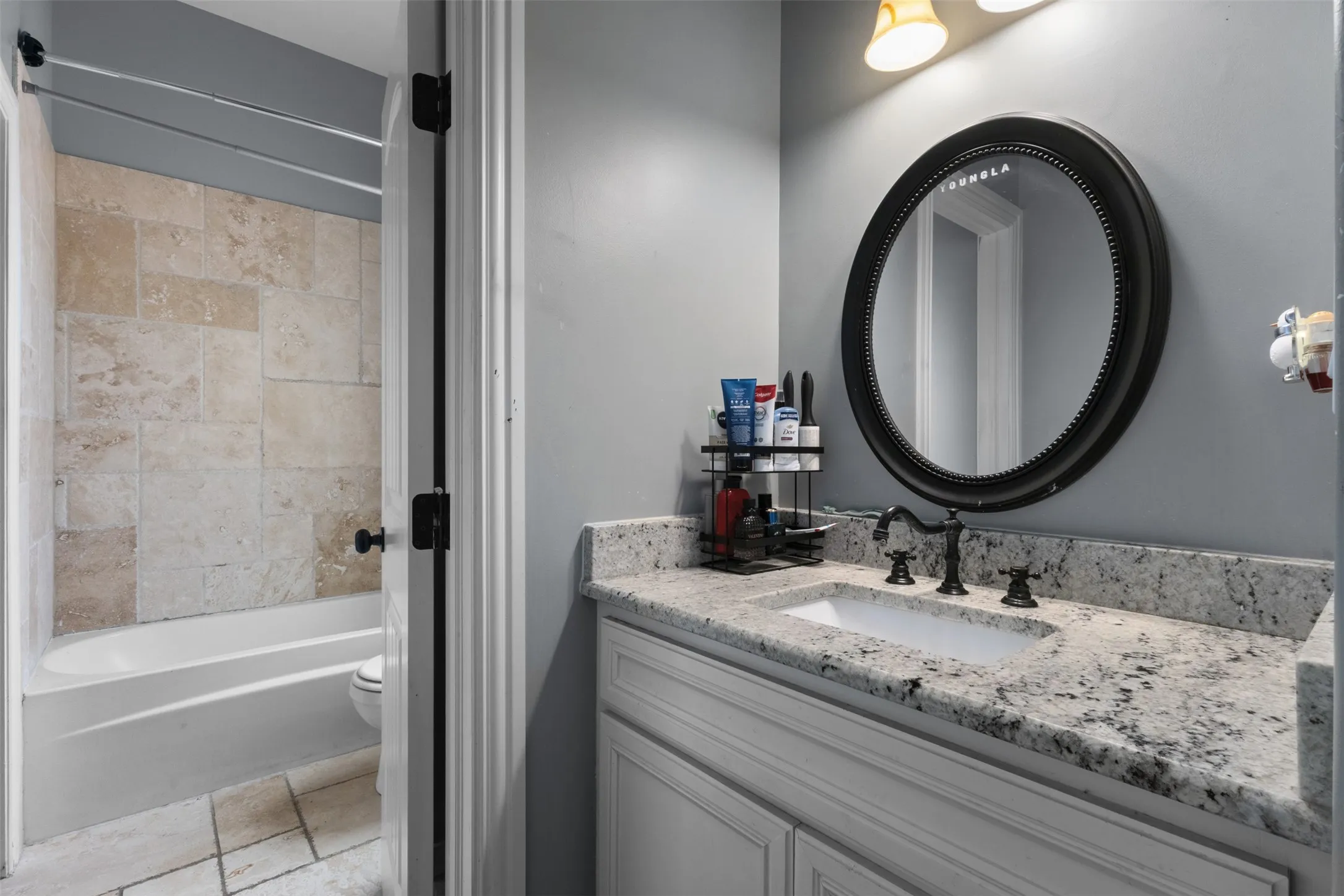 White vanity with a light-toned countertop, an undermount sink, and a black framed circular mirror