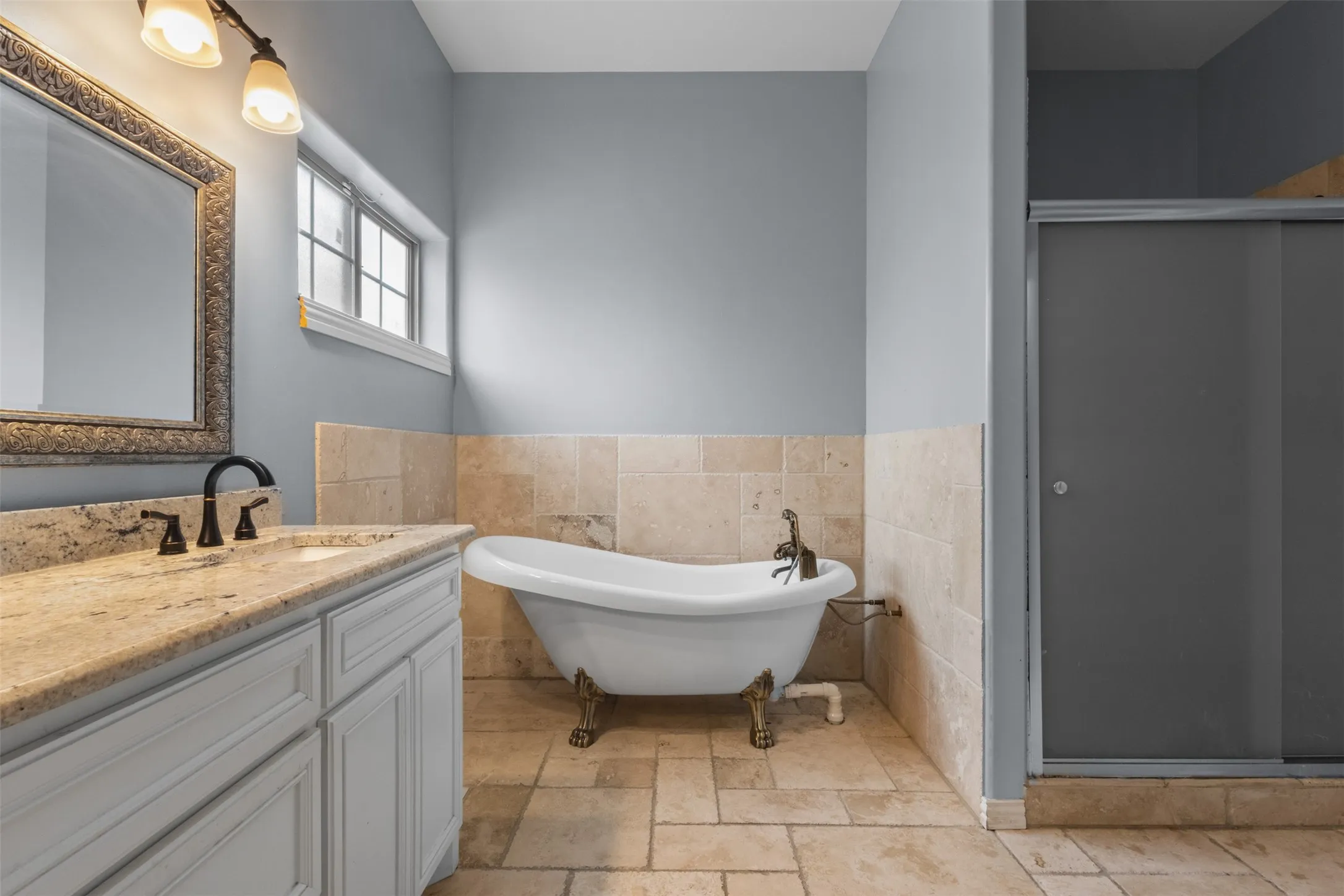 Freestanding clawfoot tub, tiled flooring, vanity with stone countertop, framed mirror, and a glass-enclosed shower