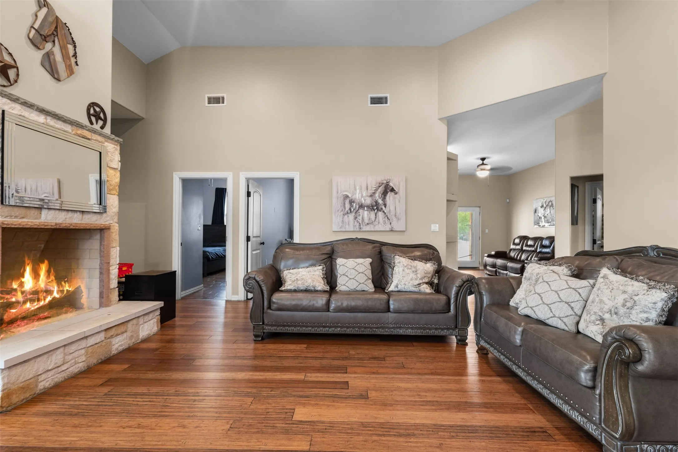 Hardwood flooring, vaulted ceilings, and a stone-clad fireplace with a hearth