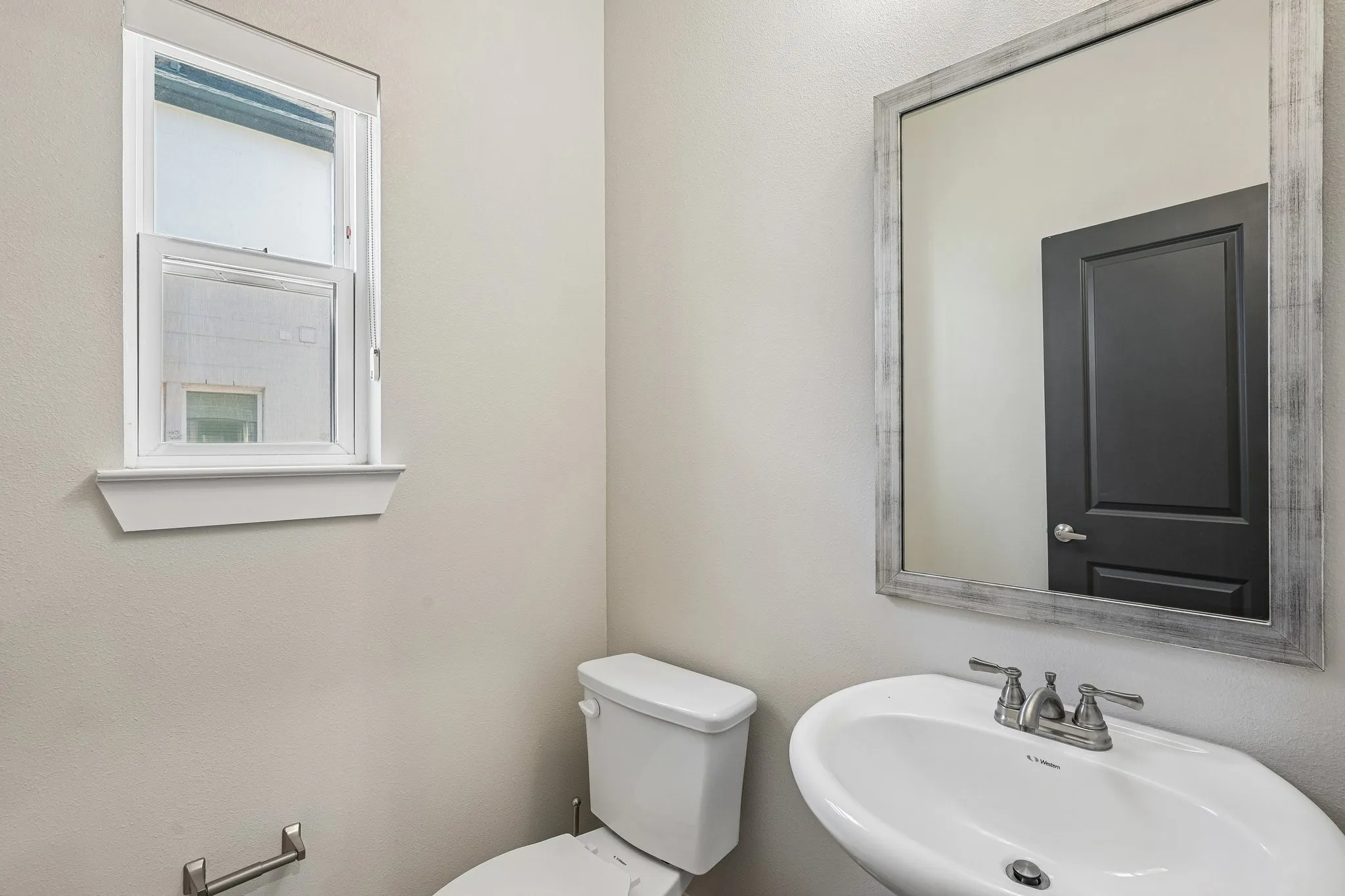 Pedestal sink with dual-handle faucet, framed mirror, and a white toilet