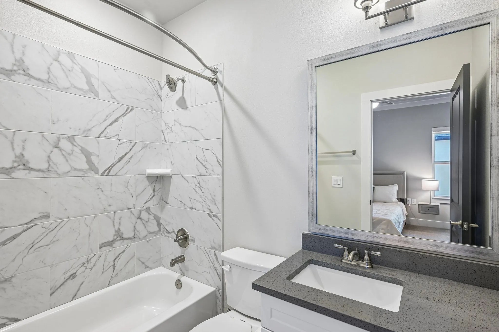 Subway tile shower surround with white tub, vanity with a dark countertop and undermount sink, framed mirror, and brushed nickel fixtures