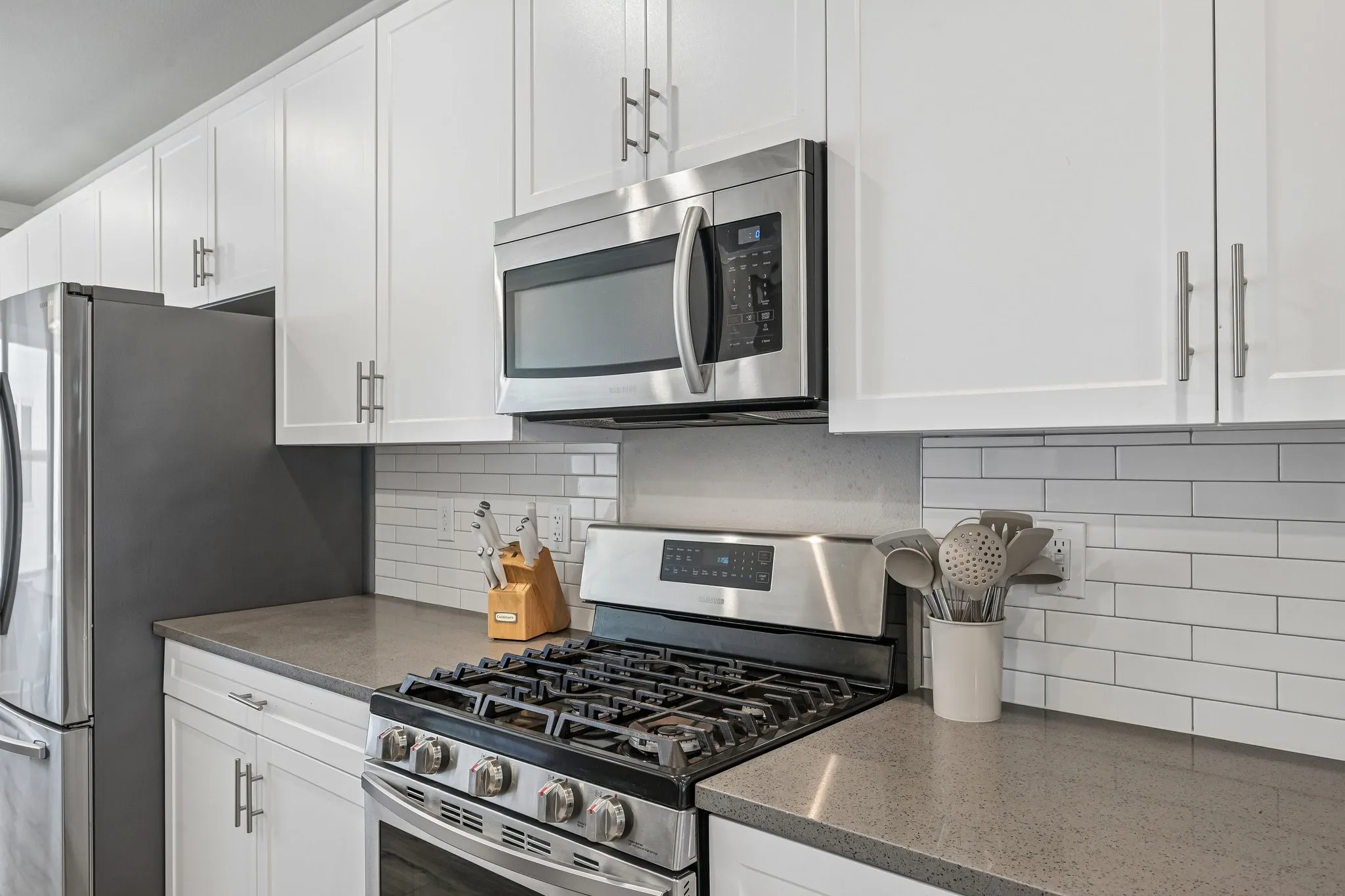 Stainless steel appliances, white shaker-style cabinetry, quartz countertops, and a white subway tile backsplash