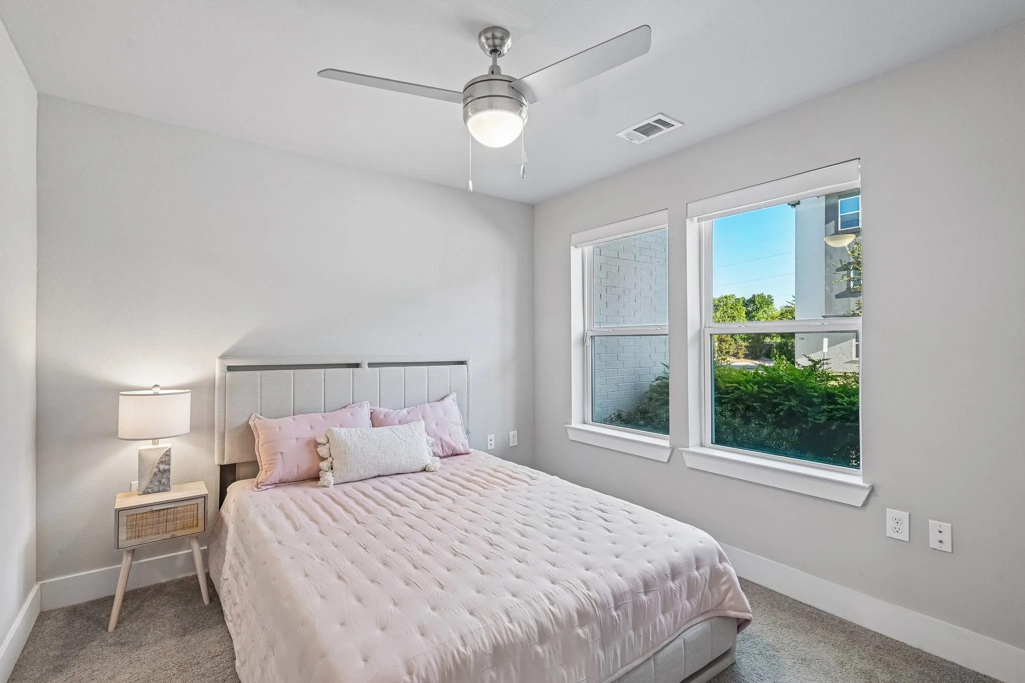 Gray carpet flooring, two windows with white trim, a ceiling fan with integrated lighting, and light gray walls