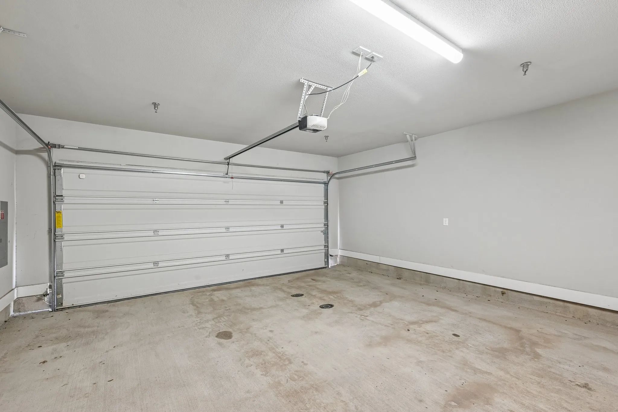 Attached garage with a white sectional door, automatic opener, concrete flooring, and overhead strip lighting