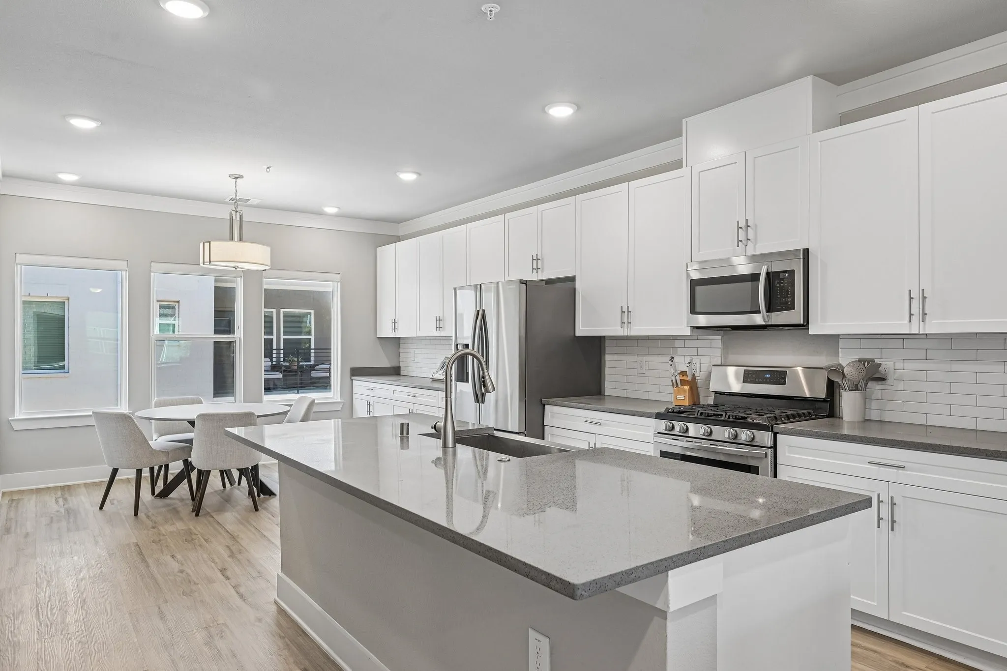 Kitchen featuring a large island with a sink, white cabinetry, stainless steel appliances, a subway tile backsplash, and light wood-finish flooring