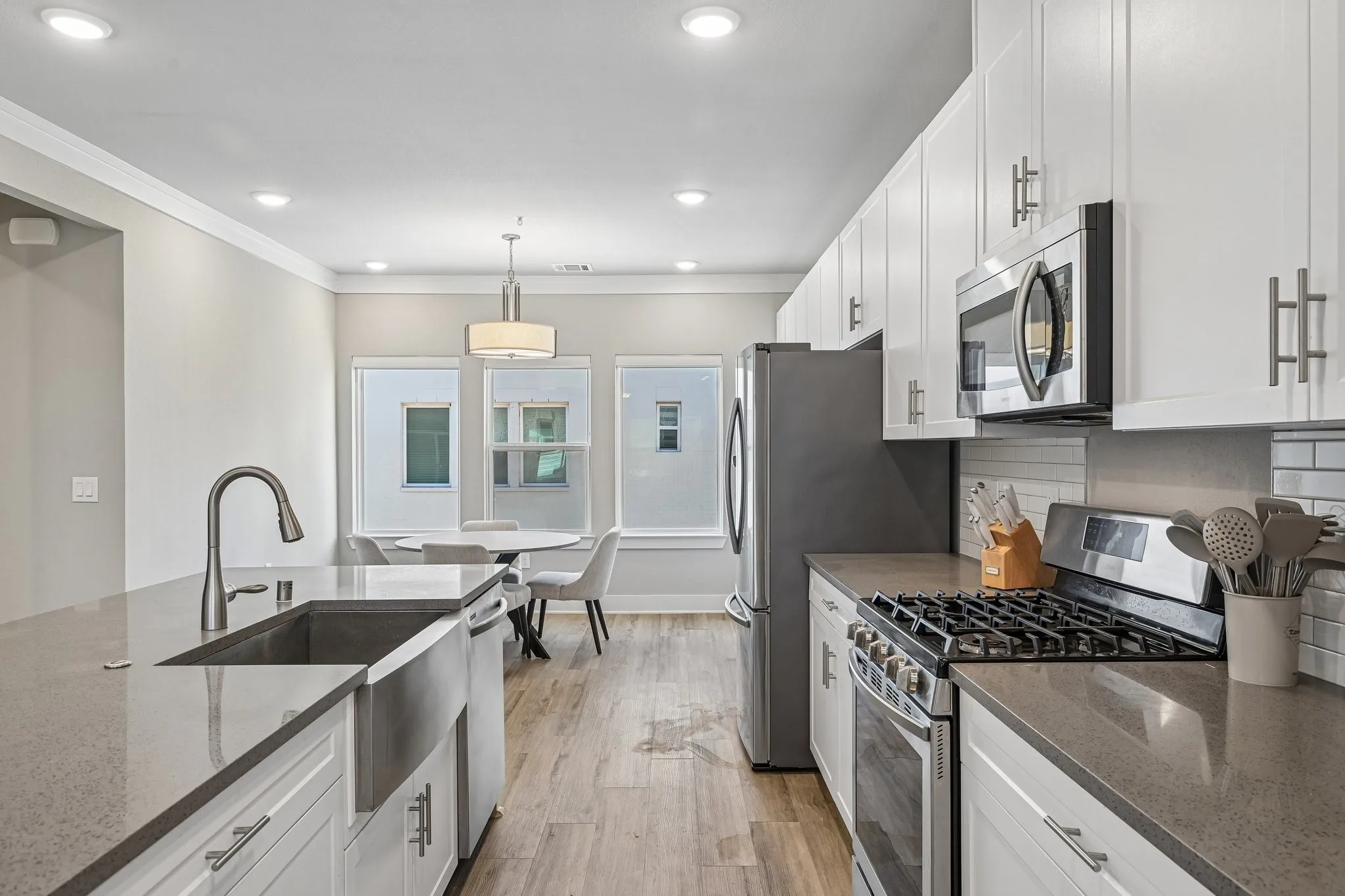 Contemporary kitchen featuring white cabinetry, stainless steel appliances, light-toned countertops, wood-finish flooring, and recessed lighting