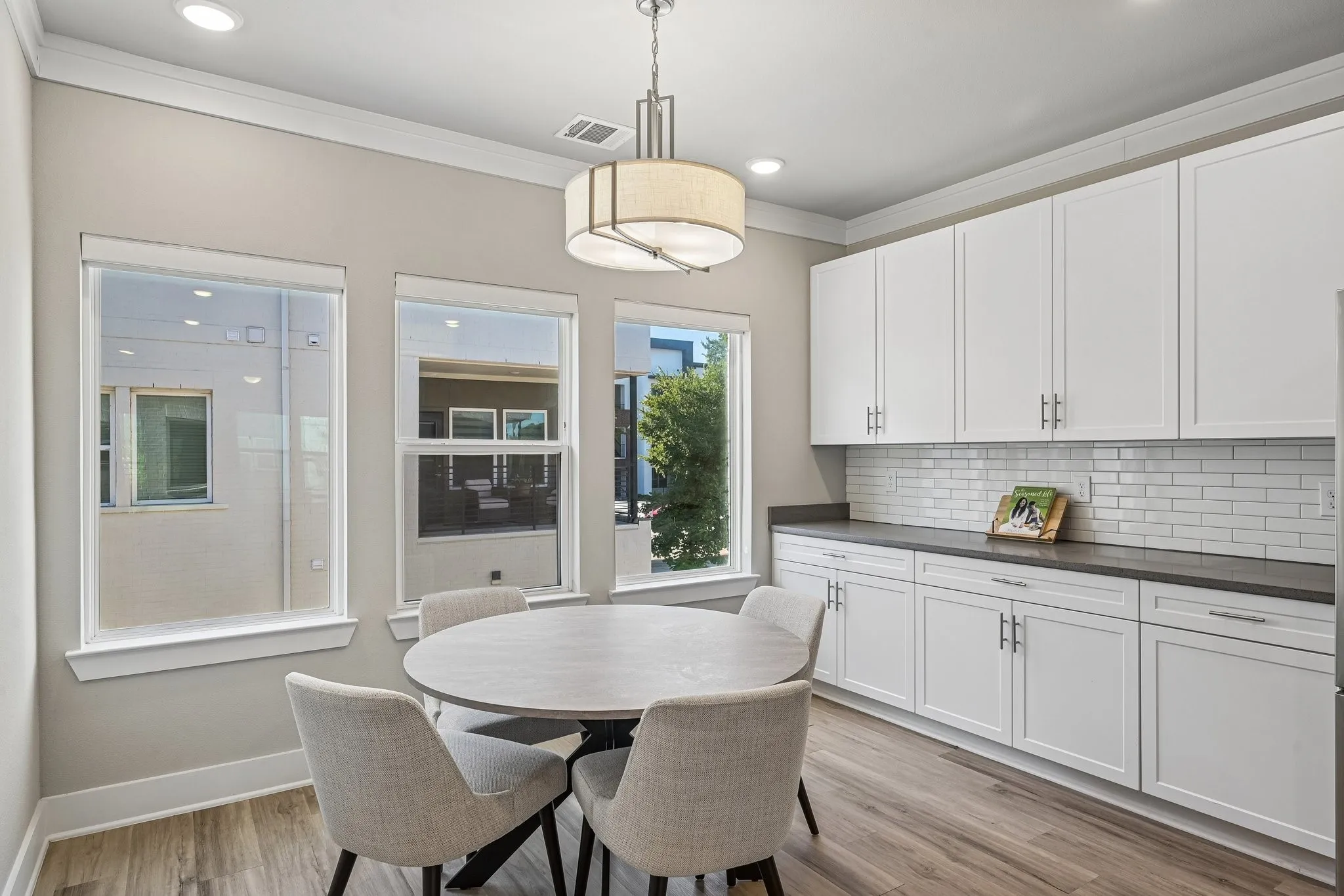 White upper and lower cabinetry, white subway tile backsplash, dark countertops, wood-finish flooring, and crown molding