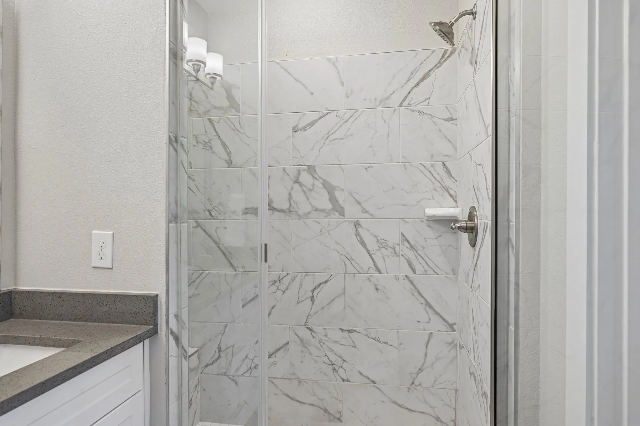 Shower with white marble-look tile, glass enclosure, and brushed nickel fixtures