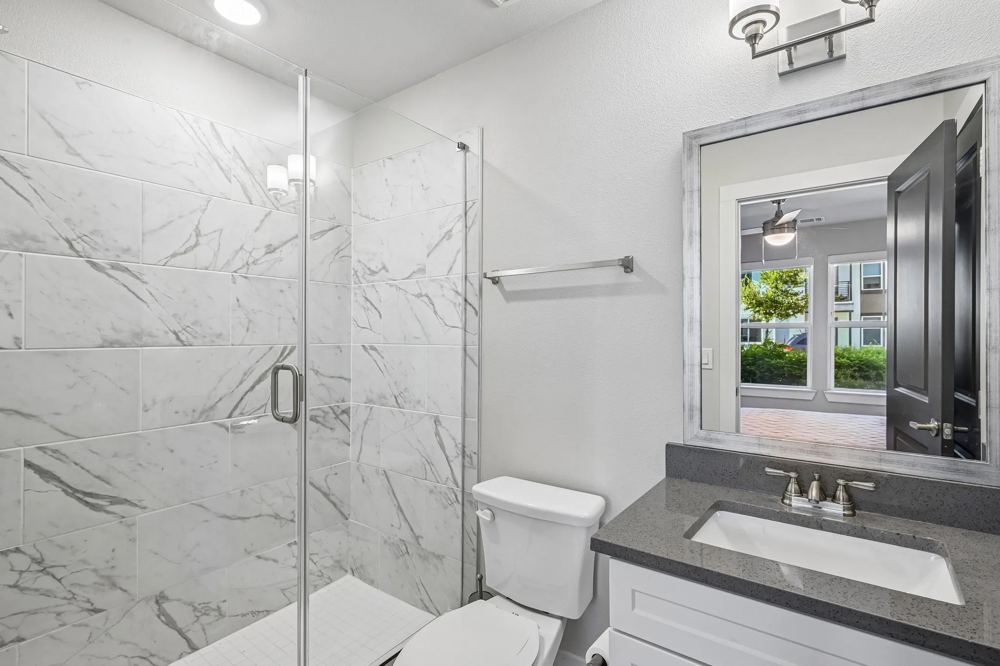 Glass-enclosed shower with large format tile surround, vanity with a rectangular undermount sink, and a dark-toned countertop