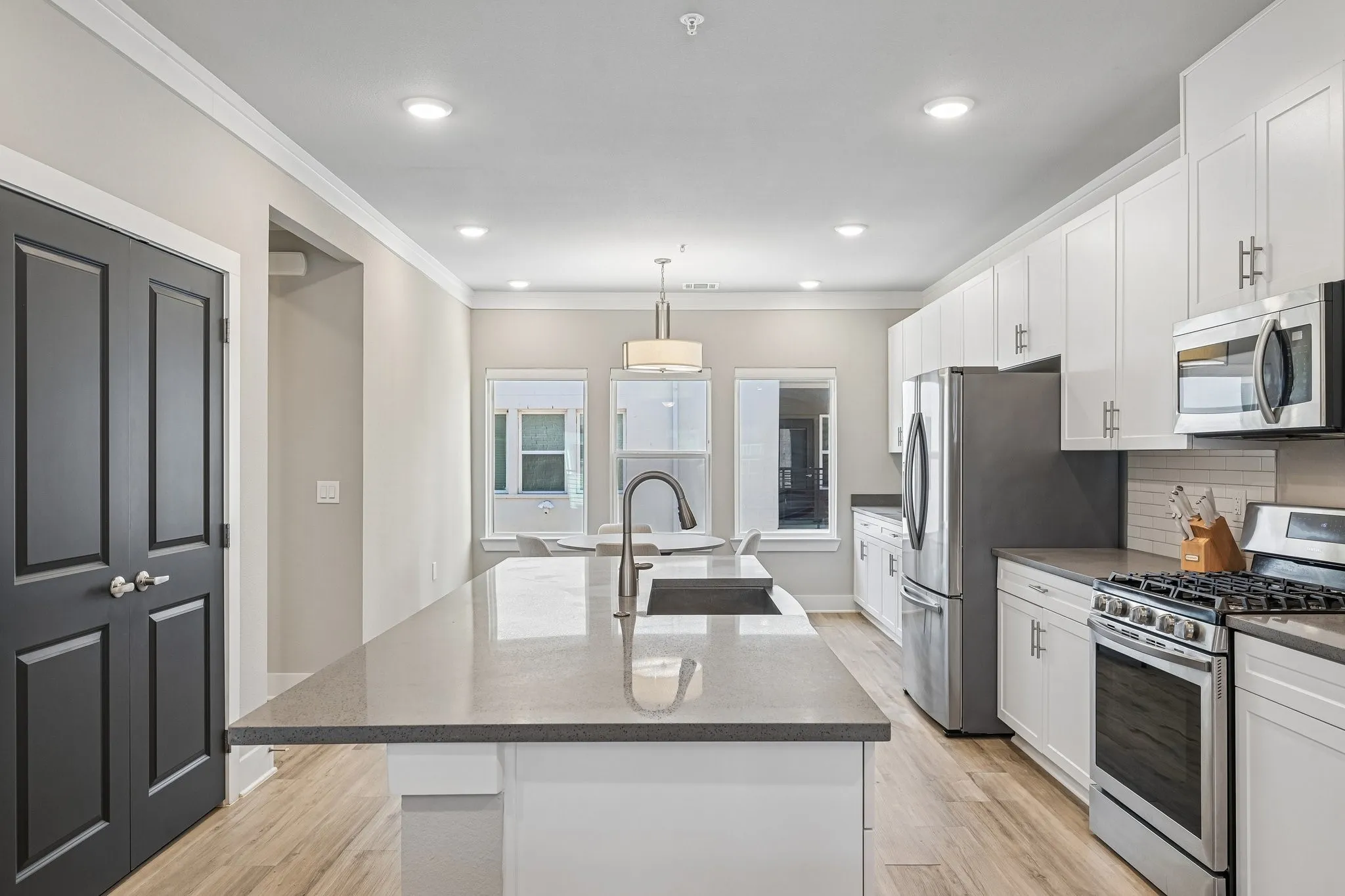 Kitchen featuring a large island with sink, white shaker cabinetry, stainless steel appliances, and wood-finish flooring