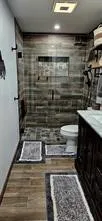 Tiled shower with a niche and glass enclosure, dark wood-finish vanity with a light-toned countertop, and wood-finish flooring