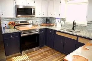 Well-appointed kitchen featuring white upper cabinetry, dark lower cabinetry, stainless steel appliances, granite countertops, and wood-finish flooring