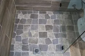 Patterned floor tiling with a square drain, complemented by wood-finish wall tiles and a clear glass shower enclosure