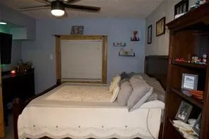 Ceiling fan with integrated lighting, wood-framed window with blinds, wall-mounted shelving, built-in shelving unit, and wall-mounted television