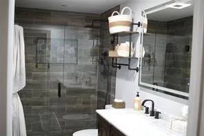 Glass-enclosed shower with subway tile surround, single vanity with a white countertop and dark-finish cabinetry, and industrial-style open shelving