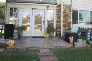 Poured concrete patio with a brick paver pathway, dual glass panel doors, and exterior stone accenting