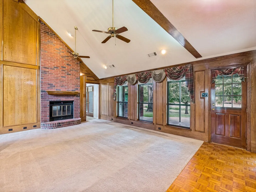 Vaulted ceiling with brick fireplace with wood mantle, wood-paneled walls, multiple windows, and wood-finish flooring
