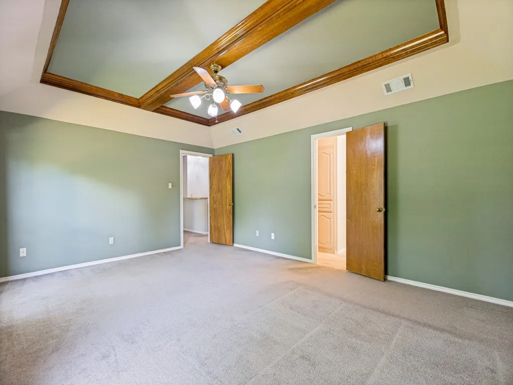 Tray ceiling with wood-finish beams, ceiling fan, looking into primary bathroom.