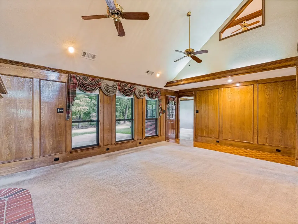 Vaulted ceiling with brick fireplace with wood mantle, wood-paneled walls, multiple windows, carpet and wood-finish flooring