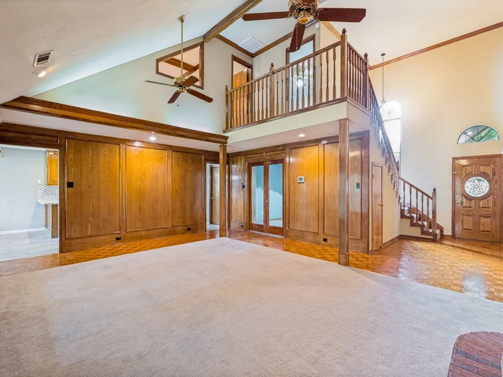 Vaulted ceilings with wood-paneled walls, a second-story interior balcony, and a wood entry door with decorative glass