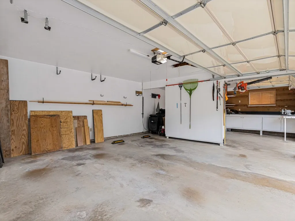 Spacious 3 car garage with concrete flooring, overhead garage door, built-in cabinetry, and work bench in 3rd bay.