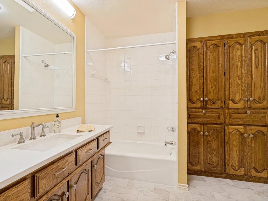 Secondary bath with quartz countertop and integrated sink, chrome-finish faucet, tub/shower combo and wood-finish cabinetry