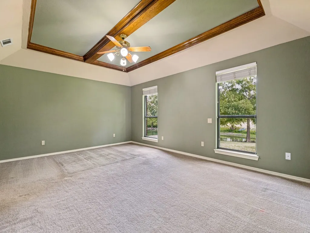 Tray ceiling with wood-finish beams, ceiling fan with integrated lighting, windows looking over back yard and pond.