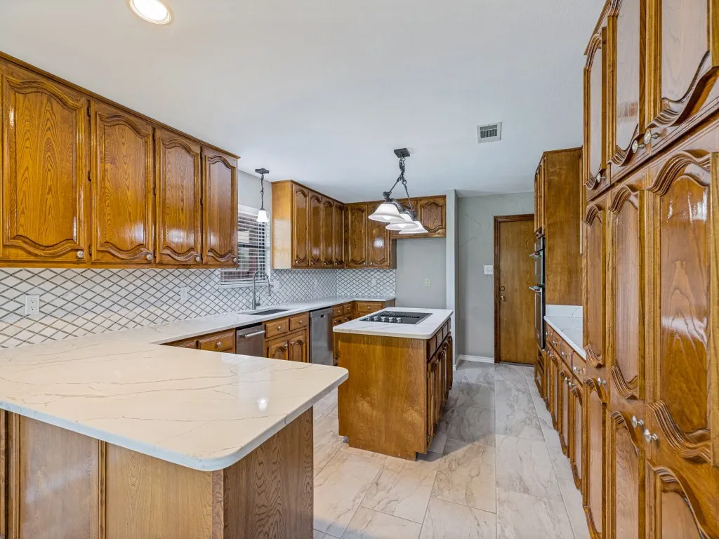 Kitchen featuring extensive cabinetry, Quartz counters, tile backsplash, and a central island with a cooktop