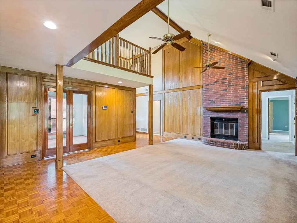 Vaulted ceiling, brick fireplace, wood paneling, and a second-story interior balcony