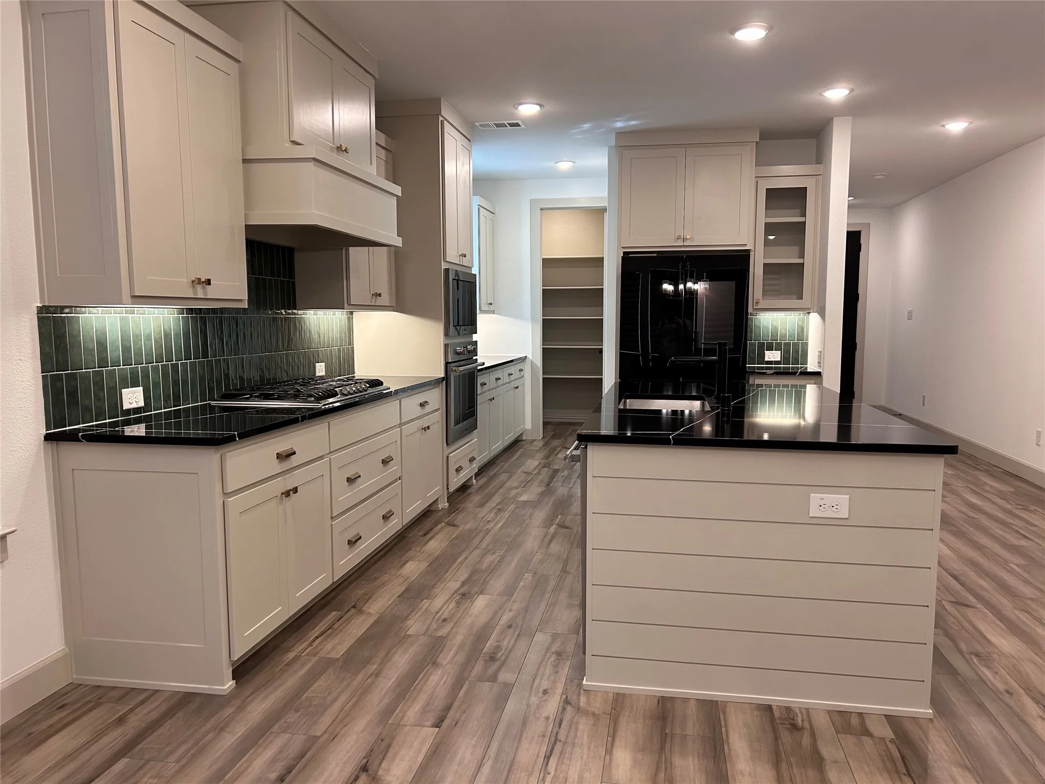 Contemporary kitchen featuring wood-finish flooring, dark countertops, light cabinetry, and an island with shiplap-style paneling