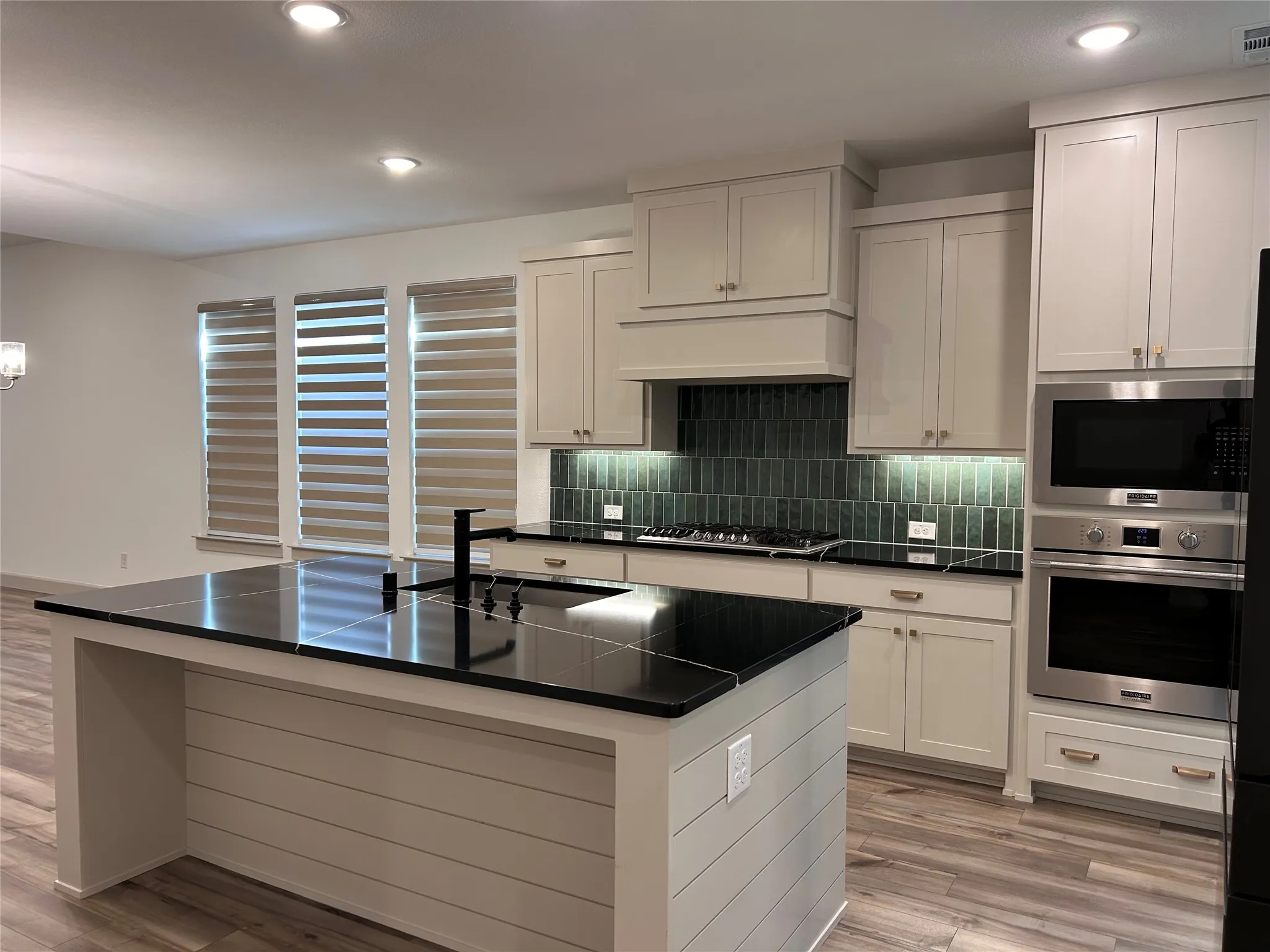 Kitchen featuring an expansive island with a dark countertop, white shaker-style cabinetry, stainless steel appliances, and wood-finish flooring