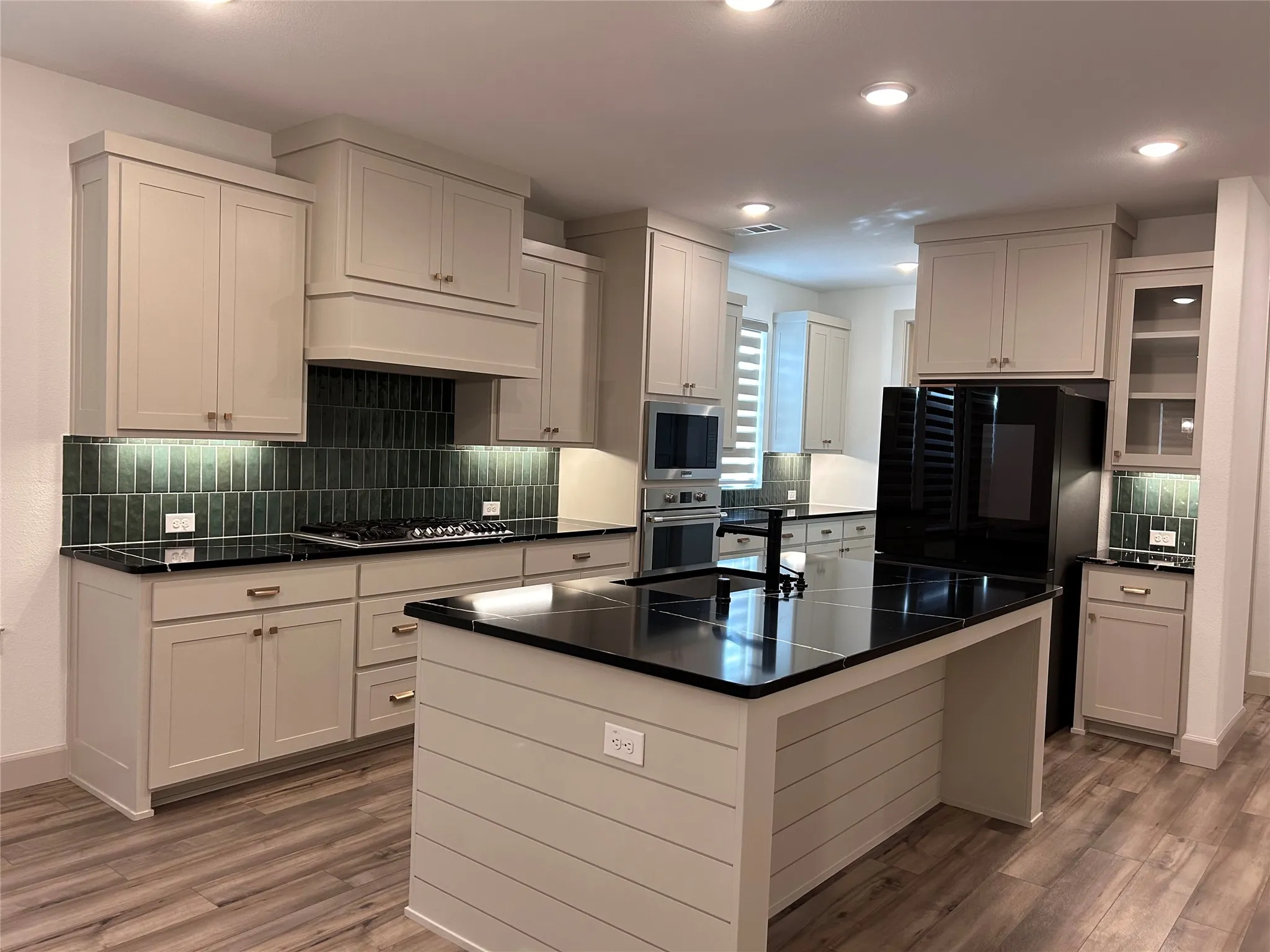 Kitchen featuring light-toned cabinetry, dark countertops, a tile backsplash, and wood-finish flooring