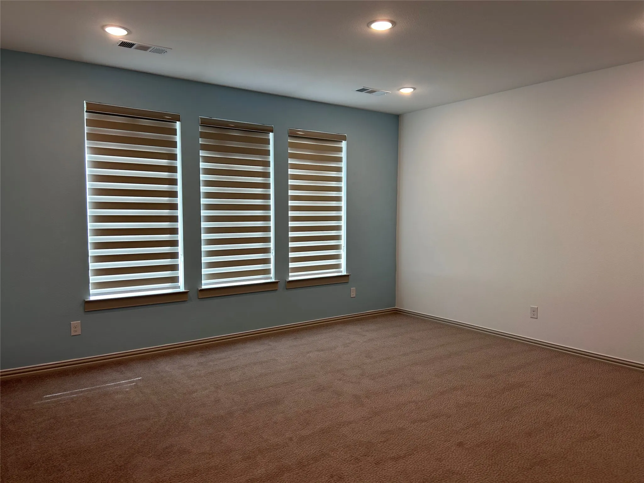Recessed lighting, three windows with blinds, and carpeted flooring