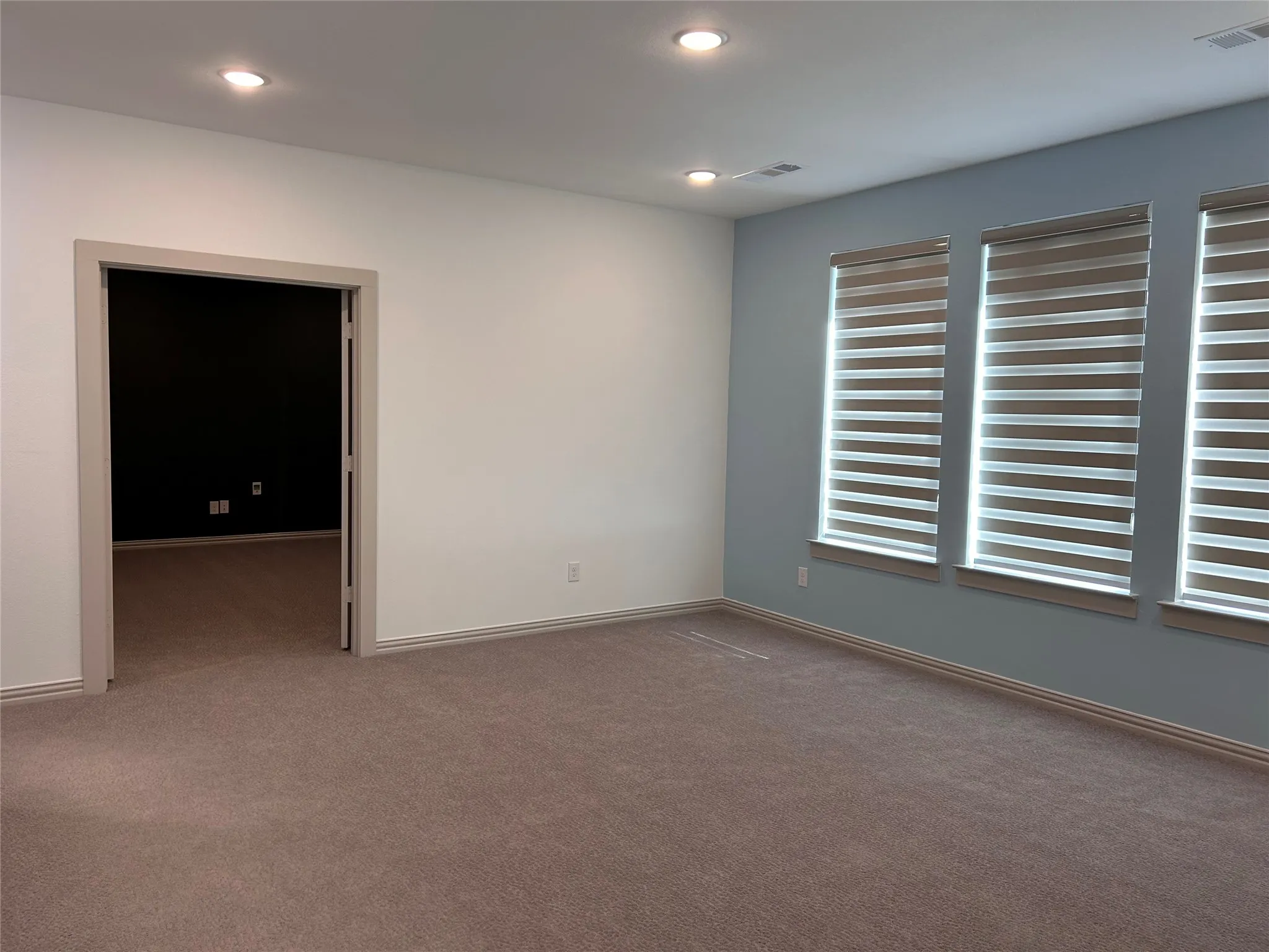 Recessed ceiling lighting, three windows with horizontal blinds, carpeted flooring, and a neutral color palette