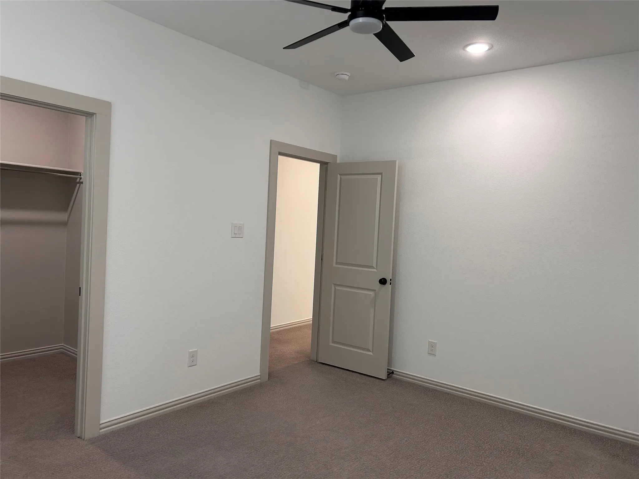 Recessed ceiling lighting, ceiling fan with black blades, neutral tone carpet flooring, light-colored walls, and a closet with a hanging rod