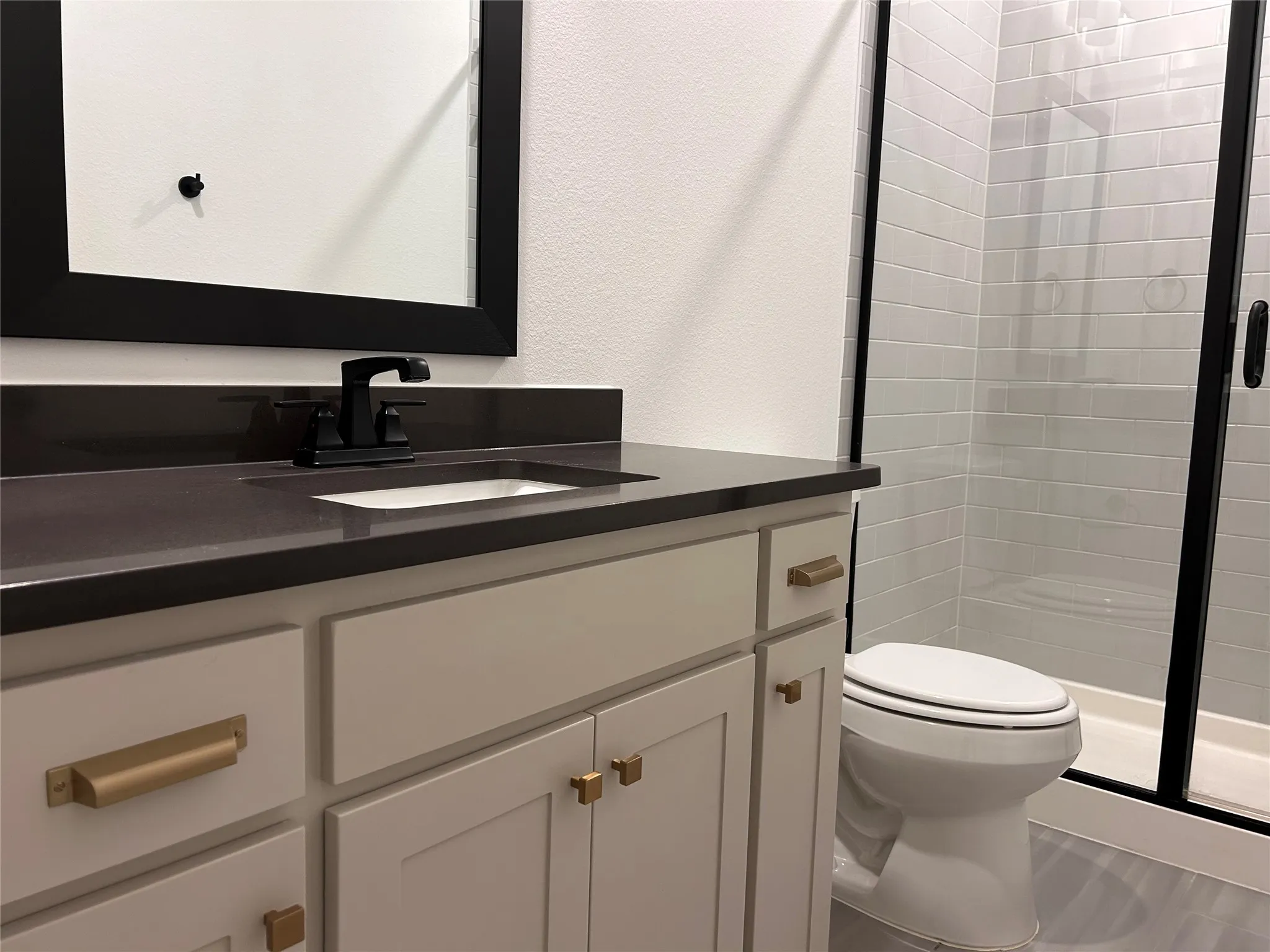 Bathroom vanity with dark countertop, integrated sink, and matte black faucet