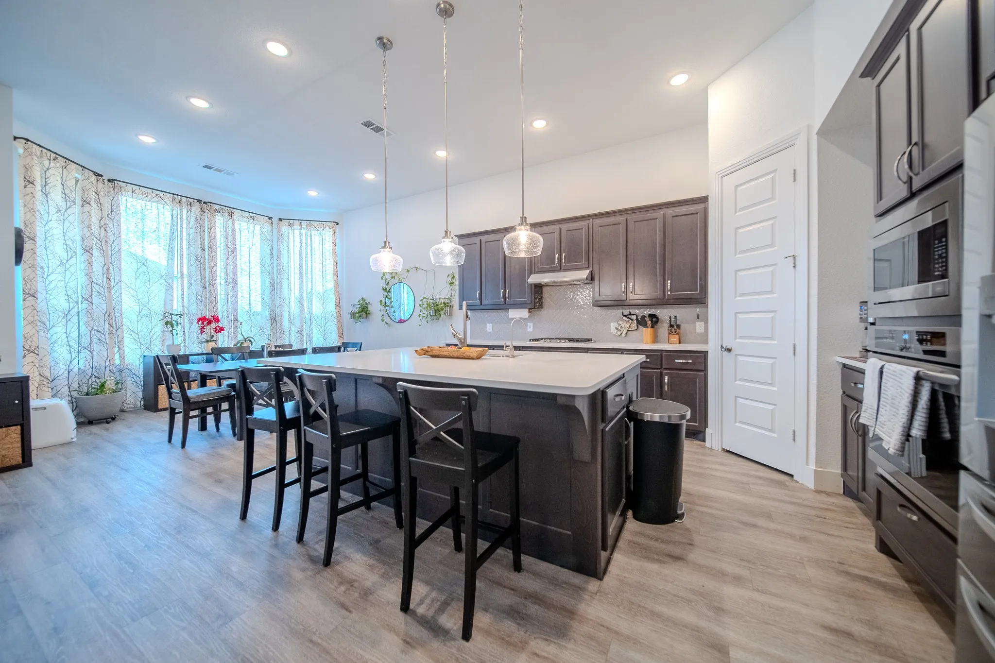 Kitchen featuring an expansive island with seating, dark wood-finish cabinetry, stainless steel appliances, and wood-finish flooring