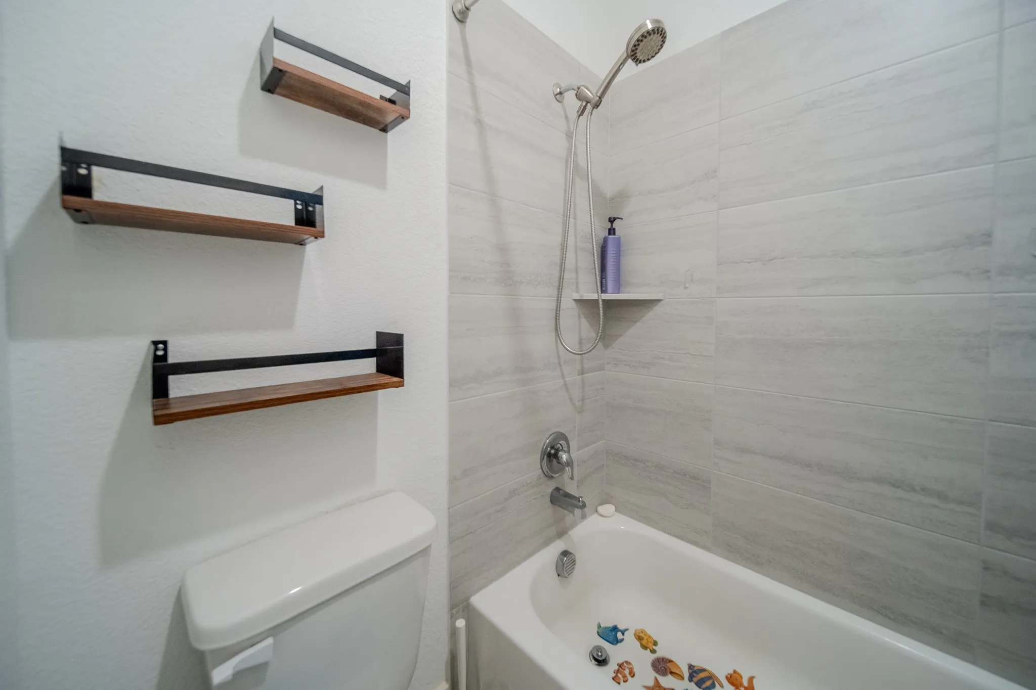 Bathtub with wall-mounted showerhead, light-toned tile surround, and an integrated shower shelf