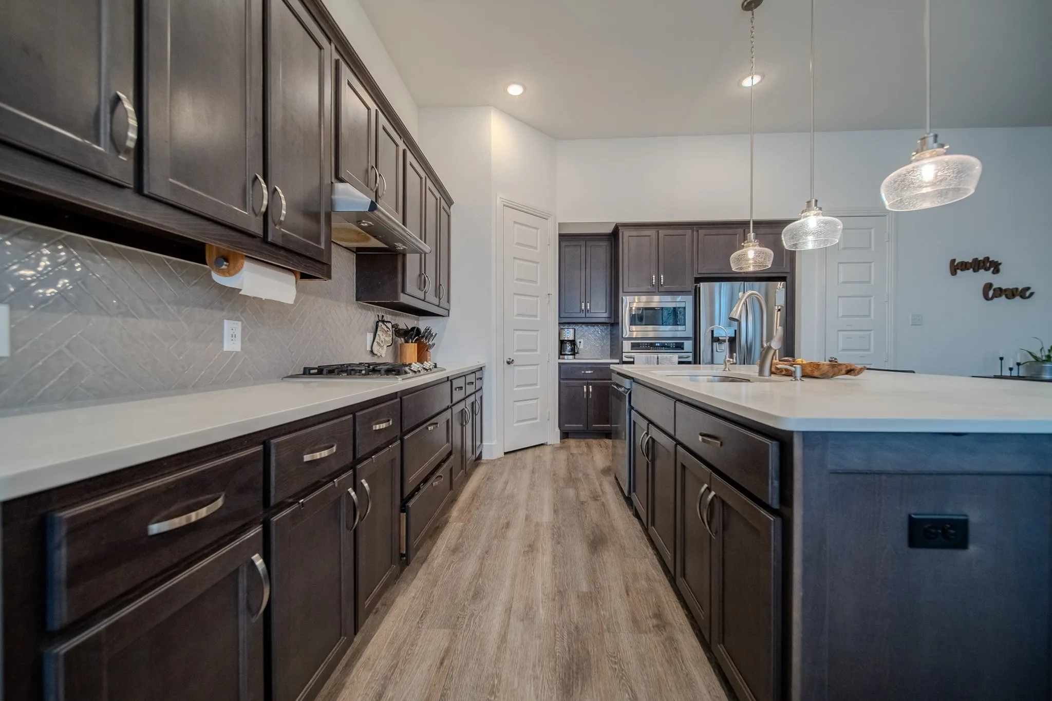 Kitchen featuring dark wood-finish cabinetry, light countertops, stainless steel appliances, a tile backsplash, and wood-finish flooring